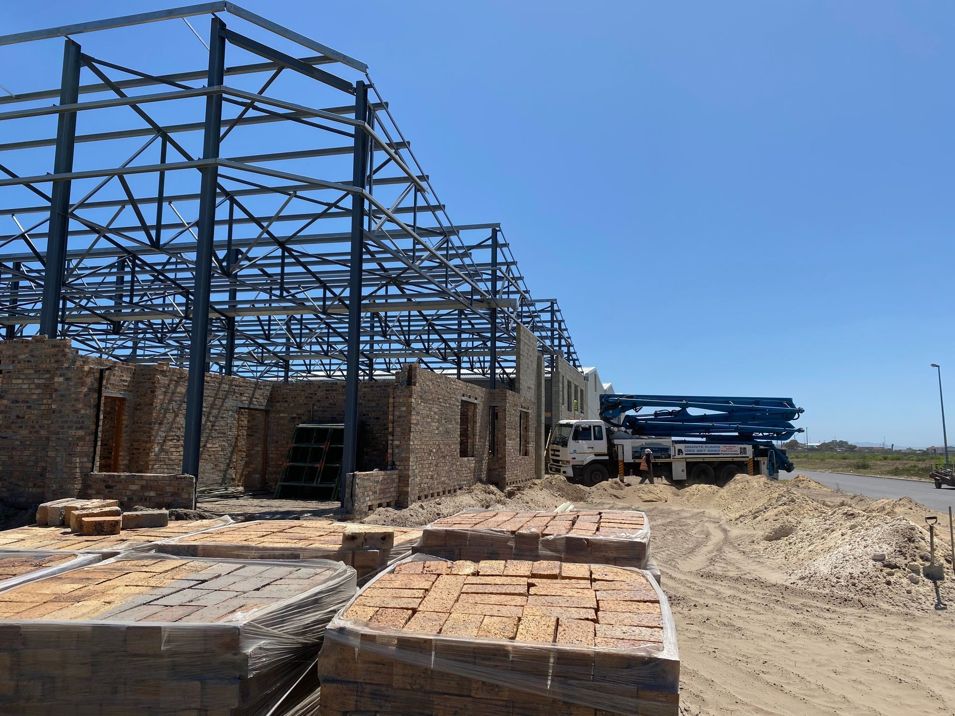 Construction site with steel frame structure and stacked bricks under a clear blue sky.
